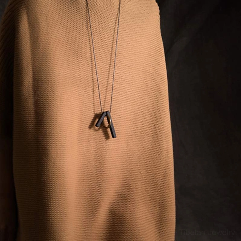 Worn ebony wood Enso necklace side profile view on tan fabric showing pendant length and waxed cord