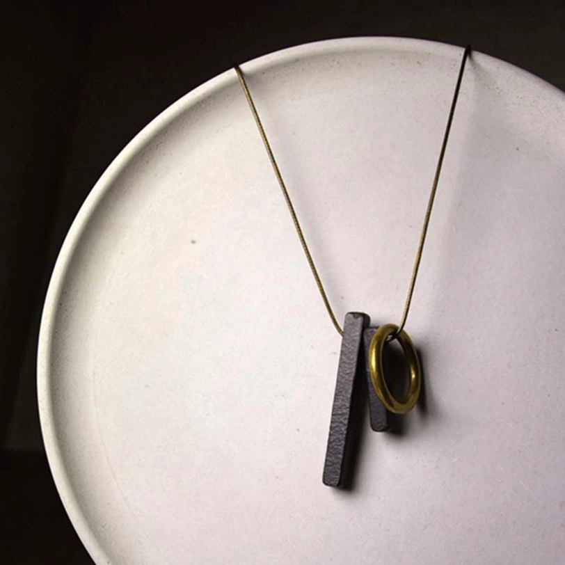 Handmade ebony wood Enso pendant close-up on white ceramic plate showing wooden details and brass ring