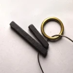 Enso zen circle ebony wood pendant necklace flat lay with brass accents on grey background