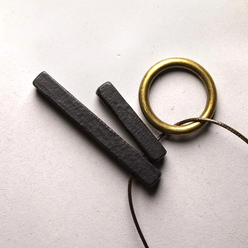 Enso zen circle ebony wood pendant necklace flat lay with brass accents on grey background