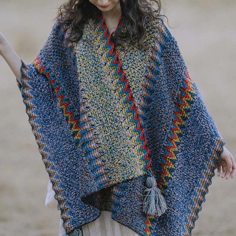 Front flat lay of knitted ethnic cape scarf displaying contrast chevron trim, tassel details and two-tone knit surface