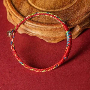 Woven Tibetan blessing bracelet displayed on wooden coaster showing braided texture and metal toggle clasp