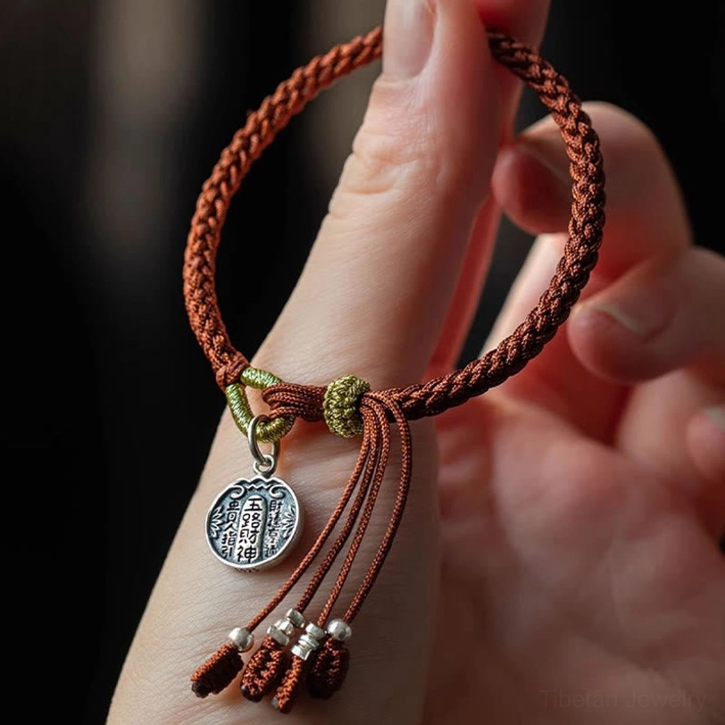 Red string wealth bracelet with sterling silver charm worn on finger, showing five directions god pendant detail