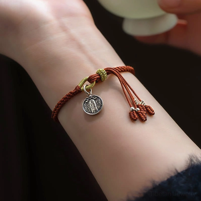 Lucky red string bracelet worn on wrist showing side view, five directions wealth god charm and braided cord design