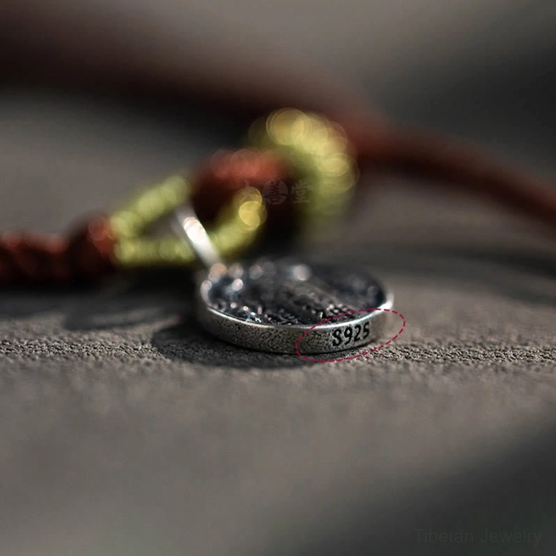 Side angle macro view of engraved silver wealth god pendant showing S925 stamp and intricate braided rope weave