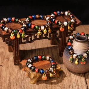 Five Elements Gold Pixiu Family Charm Liuli glass bead bracelets displayed on vintage wooden table with miniature furniture, overhead angled view showing multicolored glass beads and gold enamel pendants
