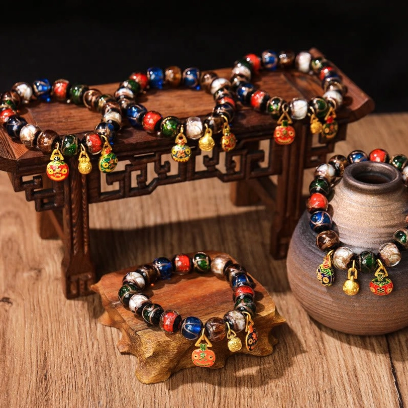 Five Elements Gold Pixiu Family Charm Liuli glass bead bracelets displayed on vintage wooden table with miniature furniture, overhead angled view showing multicolored glass beads and gold enamel pendants