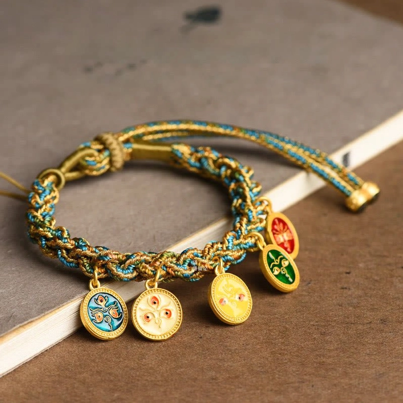 Tibetan Five God of Wealth braided string bracelet with blue-gold twisted rope and enamel deity pendants, displayed on wooden desktop with book