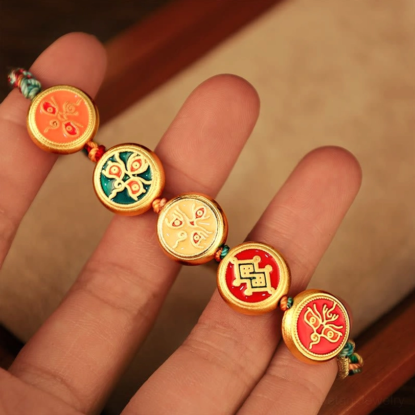 Tibetan enamel charm bracelet held between fingers displaying five unique round ethnic-style deity charms and braided rope ends
