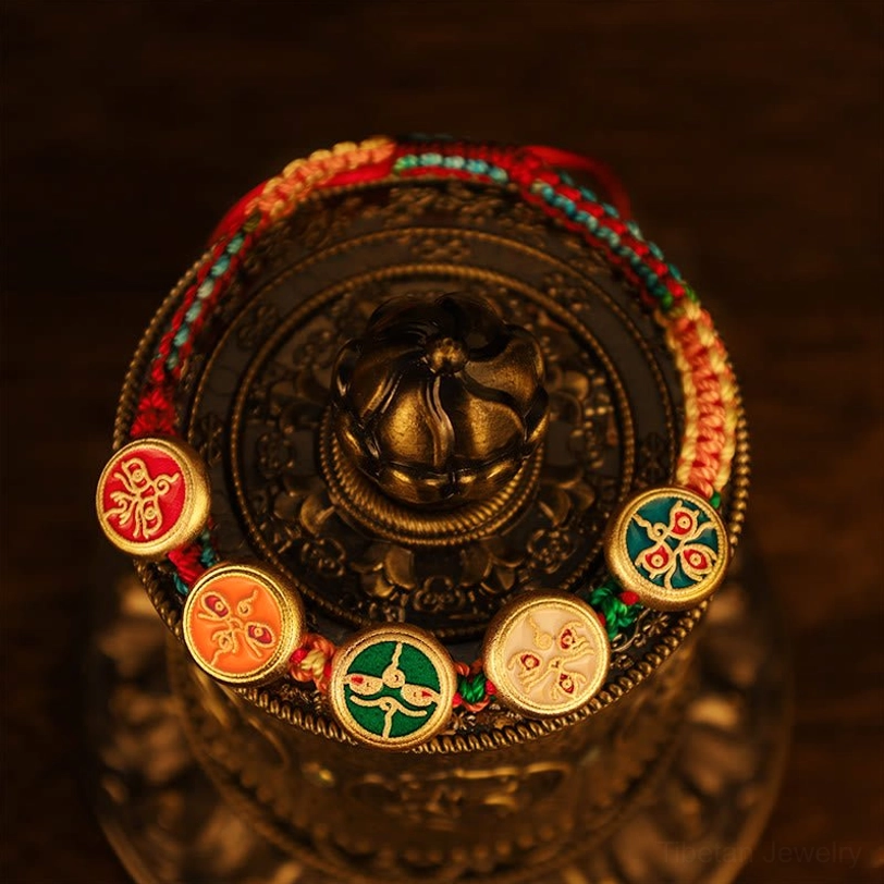 Tibetan five gods of wealth bracelet wrapped around vintage metal prayer wheel displaying braided rope and enamel charm details