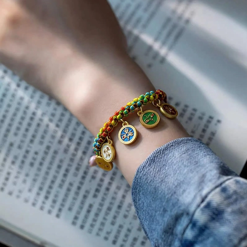 Tibetan woven luck bracelet with multicolor braided rope and dangling enamel charms worn on wrist with book background