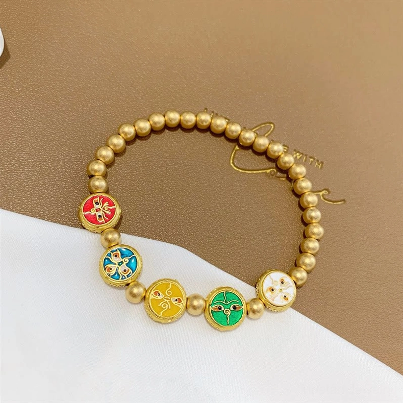 Single five gods of wealth Tibetan bracelet strand with copper beads and colorful enamel decorative charm beads on brown card with white backdrop