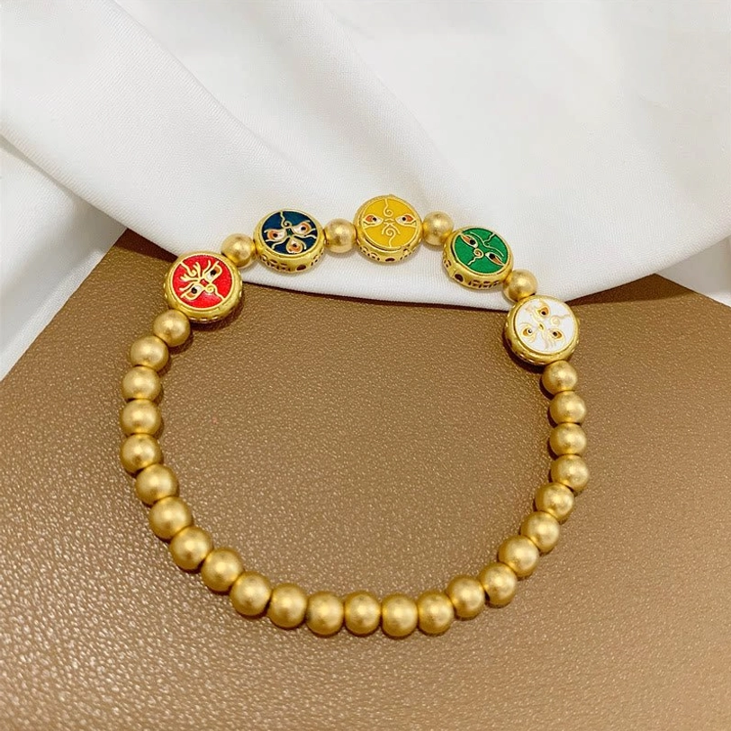Tibetan five gods of wealth luck bracelet displayed flat on brown tabletop with white fabric background, showcasing five distinct enamel deity charms