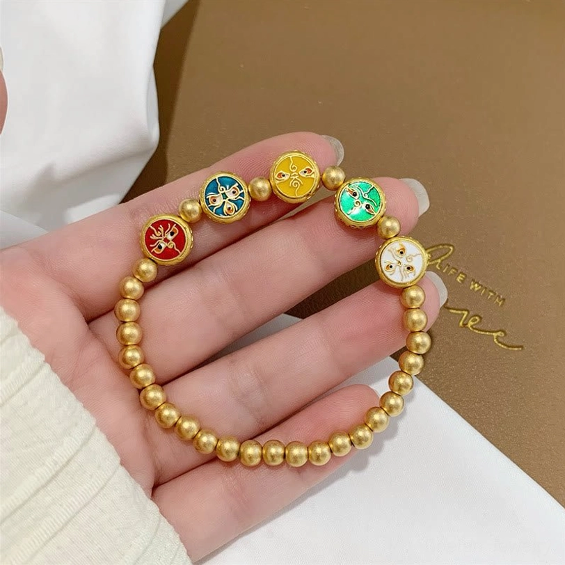 Five gods of wealth Tibetan prosperity bracelet held in hand close-up, clearly showing all five enamel charm styles on matte gold copper beads