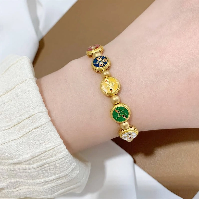 Five gods of wealth Tibetan bracelet on wrist side close-up with brown tabletop and white fabric background, partial view showing four visible enamel charms