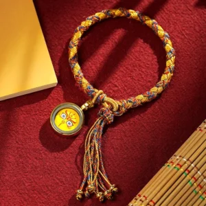 Handmade Tibetan Five Gods of Wealth bracelet with yellow-red braided rope, metal deity charm, and decorative tassel in top-down flat lay view