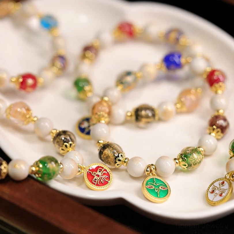 Five Gods of Wealth Tibetan bracelets featuring various enamel pendants and colored glass beads arranged on round white ceramic plate