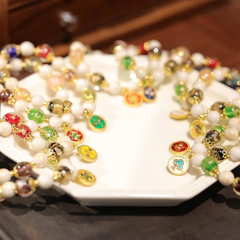Collection of Five Gods of Wealth Tibetan blessing bracelets with green glass beads and decorative enamel facial pendants on square ceramic plate