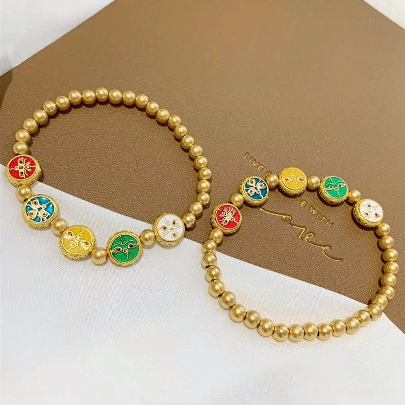 Pair of five gods of wealth Tibetan copper beads luck bracelets on brown greeting card background, matching beaded strands with enamel charms visible