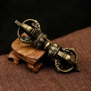 Five-prong Tibetan Vajra Dorje in antique bronze, oblique side view displaying intricate religious carvings on brown linen with wooden stand