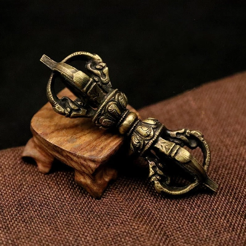 Five-prong Tibetan Vajra Dorje in antique bronze, oblique side view displaying intricate religious carvings on brown linen with wooden stand