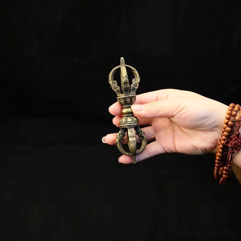Small five-prong Tibetan Vajra Dorje held in hand with Tibetan beaded bracelet on black background, showing aged bronze ritual tool finish