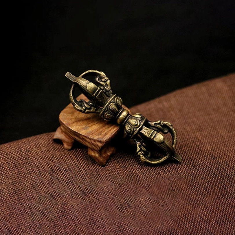 Five-prong Vajra Dorje overhead view showcasing aged bronze texture and carved decorative end rings on linen background