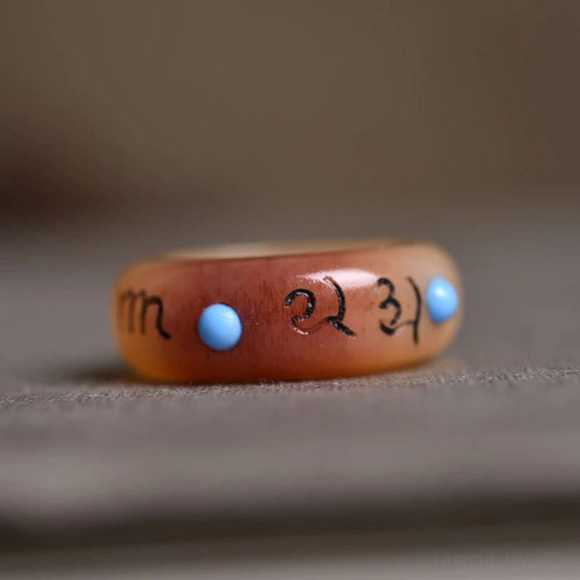 Flat camel bone ring with detailed mantra engravings and multiple blue stone bead inlays, low-angle side view showing thickness