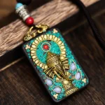 Tibetan Ganesha ebony wood pendant with turquoise inlay and gold accents, top-down close-up view
