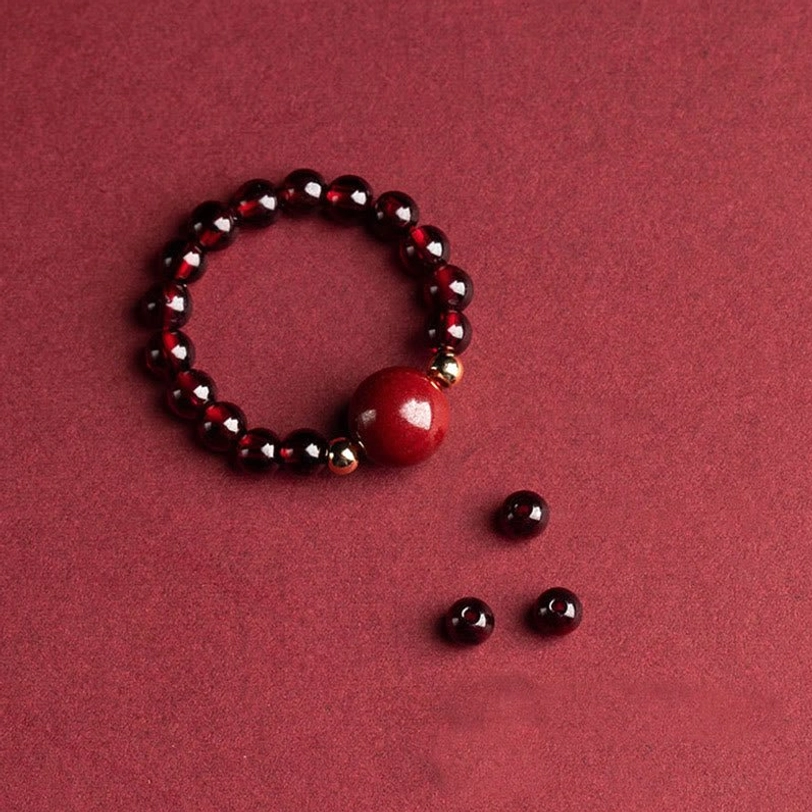 Garnet and cinnabar round bead ring with gold metal spacer details, oblique top view on solid wine red background