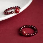 Garnet cinnabar PiXiu ring with Om Mani Padme Hum mantra engraving, displayed on white porcelain with gold metal spacer beads on wine red background