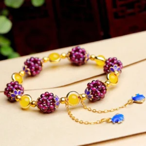 Pink Tibetan garnet cluster bracelet with yellow spacer beads and dual blue enamel drop charms on kraft paper