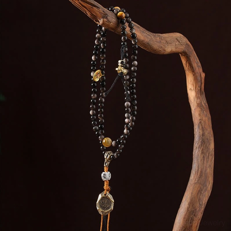 Garuda obsidian mala necklace side view dark background with tiered metal charms brown tassel