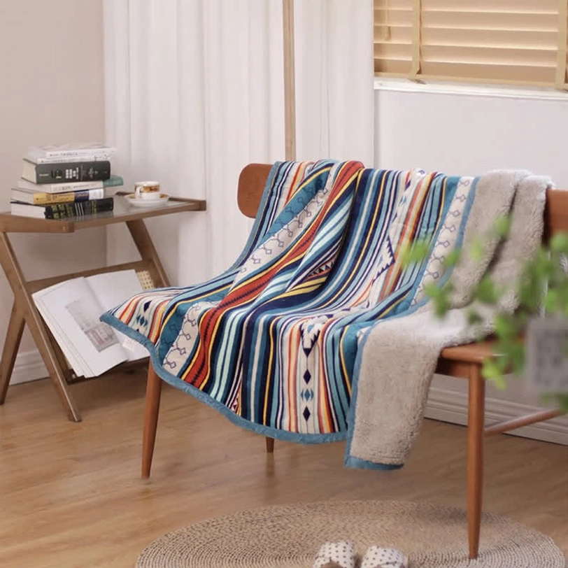 Dual-sided geometric throw blanket on wooden chair showing striped design and blue trim, perfect accent blanket for home office nook