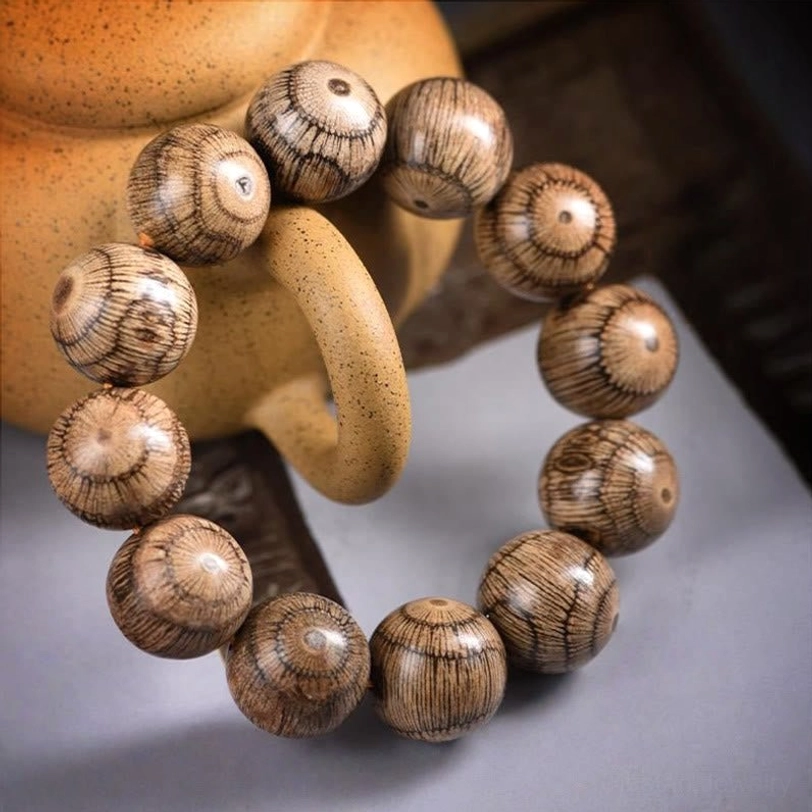 Oblique side view of Gnetum wood beaded bracelet styled with tea ware showing natural wood grain texture