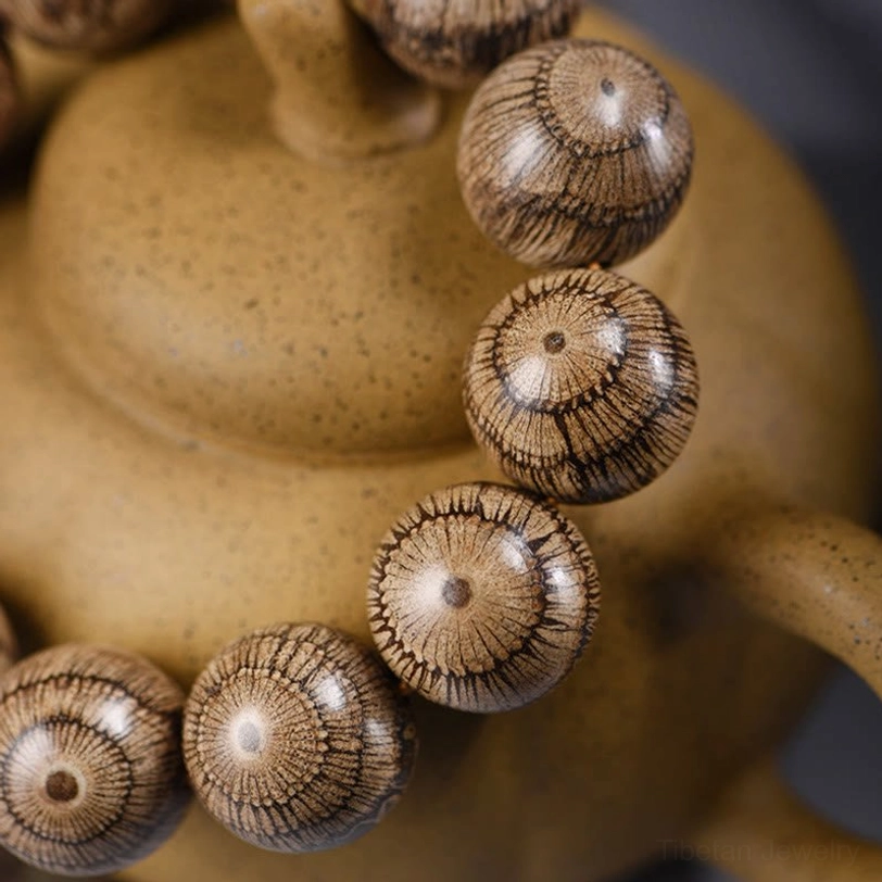 Side close-up of Gnetum wood beaded bracelet showing radial wood grain on individual beads with clay backdrop