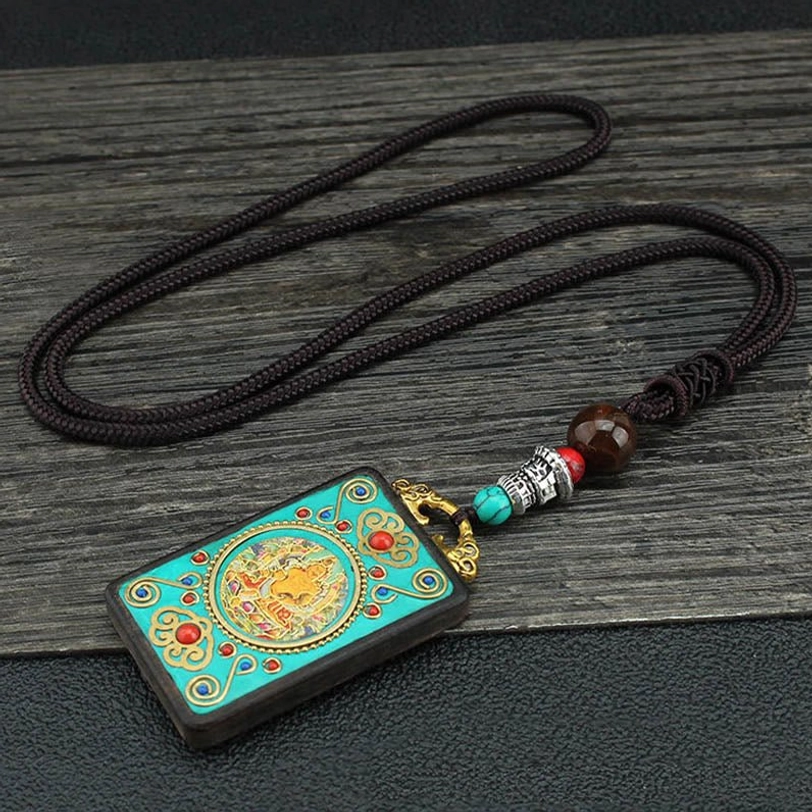 Single Five Gods of Wealth thangka pendant necklace with braided black rope, turquoise and brown bead accents on dark wooden table