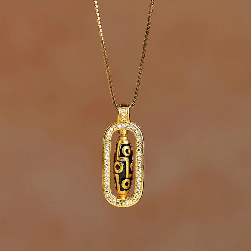 Nine-eye dzi bead pendant necklace full standing view on warm indoor background, slim gold box chain design