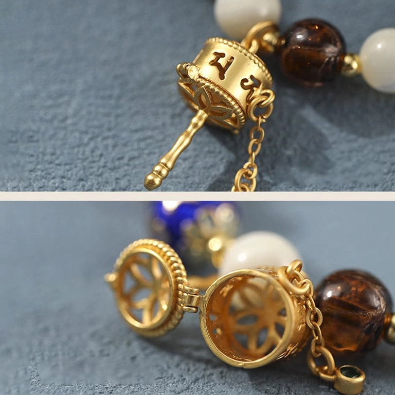 Detailed close-up of hollow gold-carved prayer wheel pendant with om mani inscriptions and chain attachment