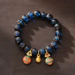 Gold Swallowing Beast blue Liuli glass fortune bracelet with cloisonne charms and gold bell on wooden surface