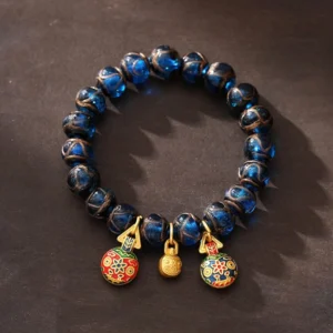 Gold Swallowing Beast blue Liuli glass fortune bracelet with cloisonne charms and gold bell on wooden surface
