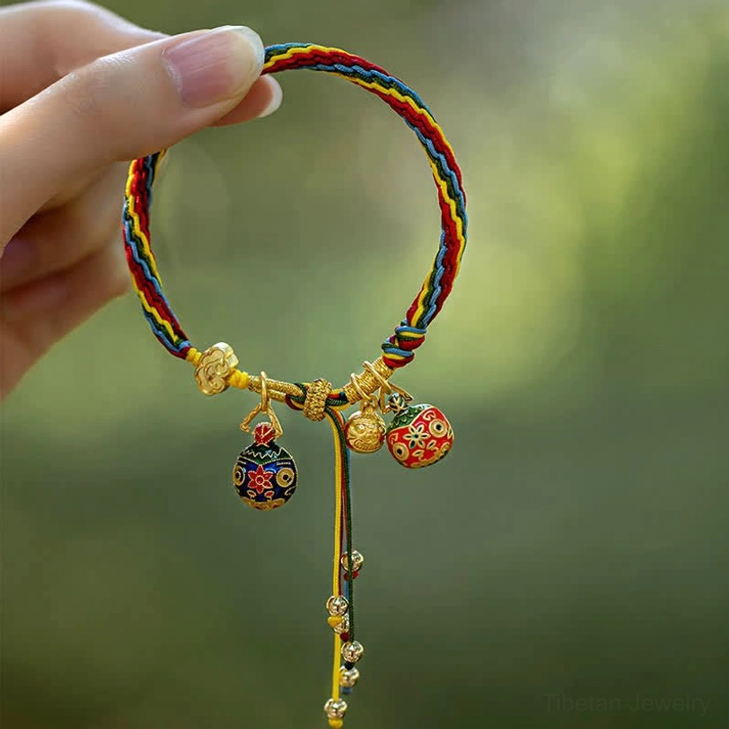Gold Swallowing Beast bracelet held by hand showing multicolor twisted rope, gold fasteners, and beaded tassel detail