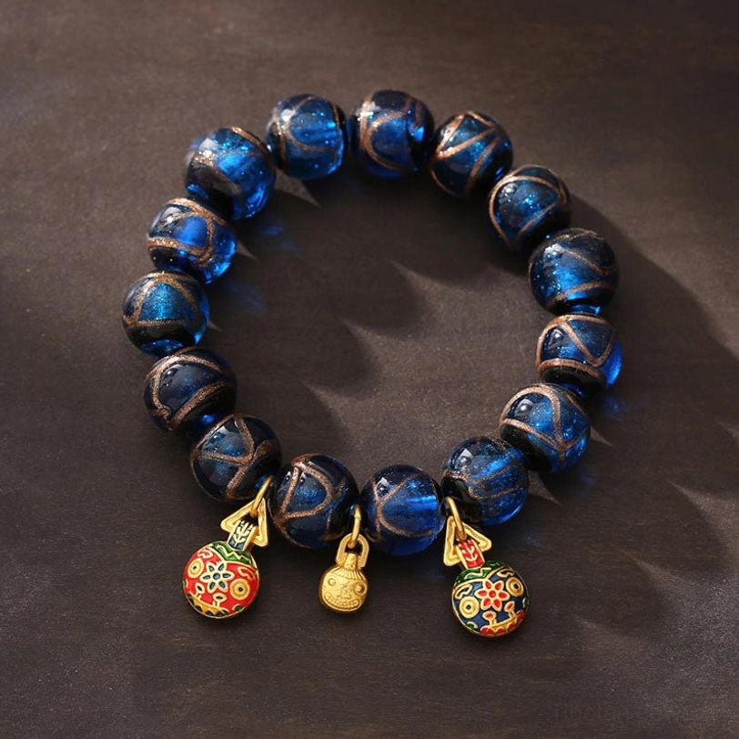 Angled top view of handmade blue Liuli glass fortune bracelet with prosperity charm set
