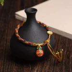 Gold Swallowing Beast Mother bracelet with multicolor woven cord, gold pendants, and protective tassel displayed on wooden desk