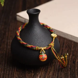 Gold Swallowing Beast Mother bracelet with multicolor woven cord, gold pendants, and protective tassel displayed on wooden desk