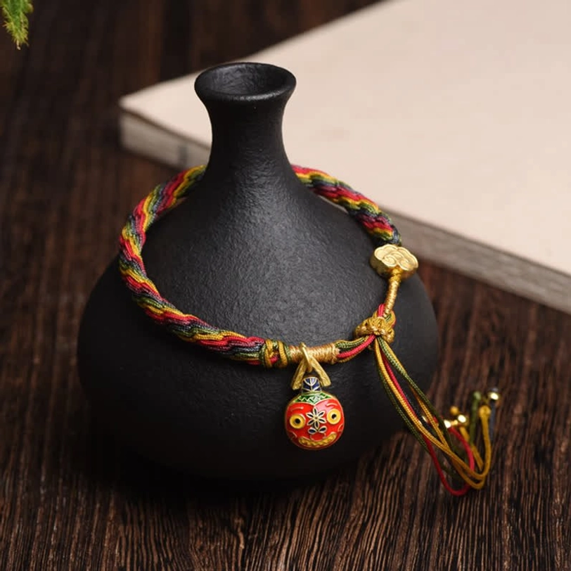 Gold Swallowing Beast Mother bracelet with multicolor woven cord, gold pendants, and protective tassel displayed on wooden desk