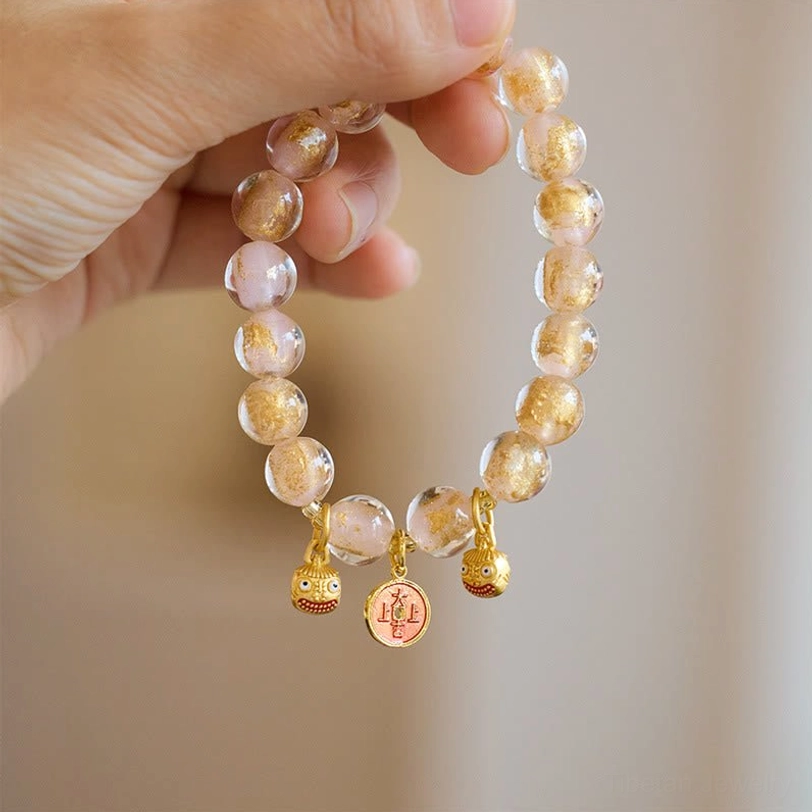 Gradient translucent pink liuli glass fortune bracelet with gold metal Pi Xiu pendants, close-up hand view