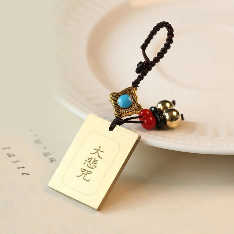 Great Compassion Mantra brass tag keychain with engraved Buddhist mantra characters on white ceramic plate, spiritual protection charm