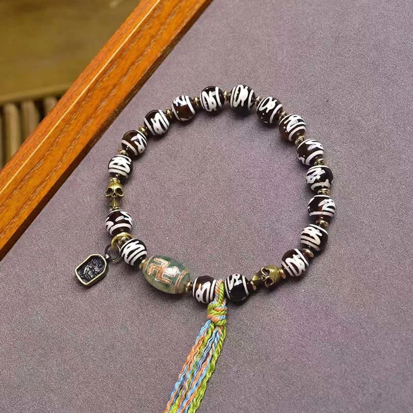 Green agate Dzi bead wealth bracelet with multicolor woven tassel and metal square pendant on purple fabric
