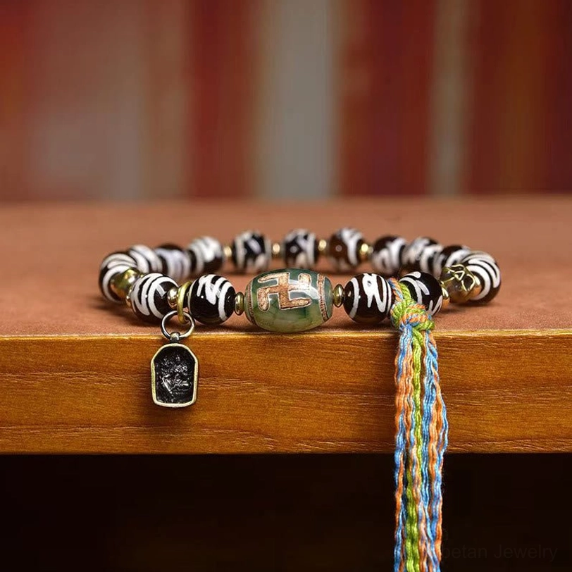 Green agate Tibetan Dzi bead bracelet side view with metal accent charm and multicolor tassel on wood
